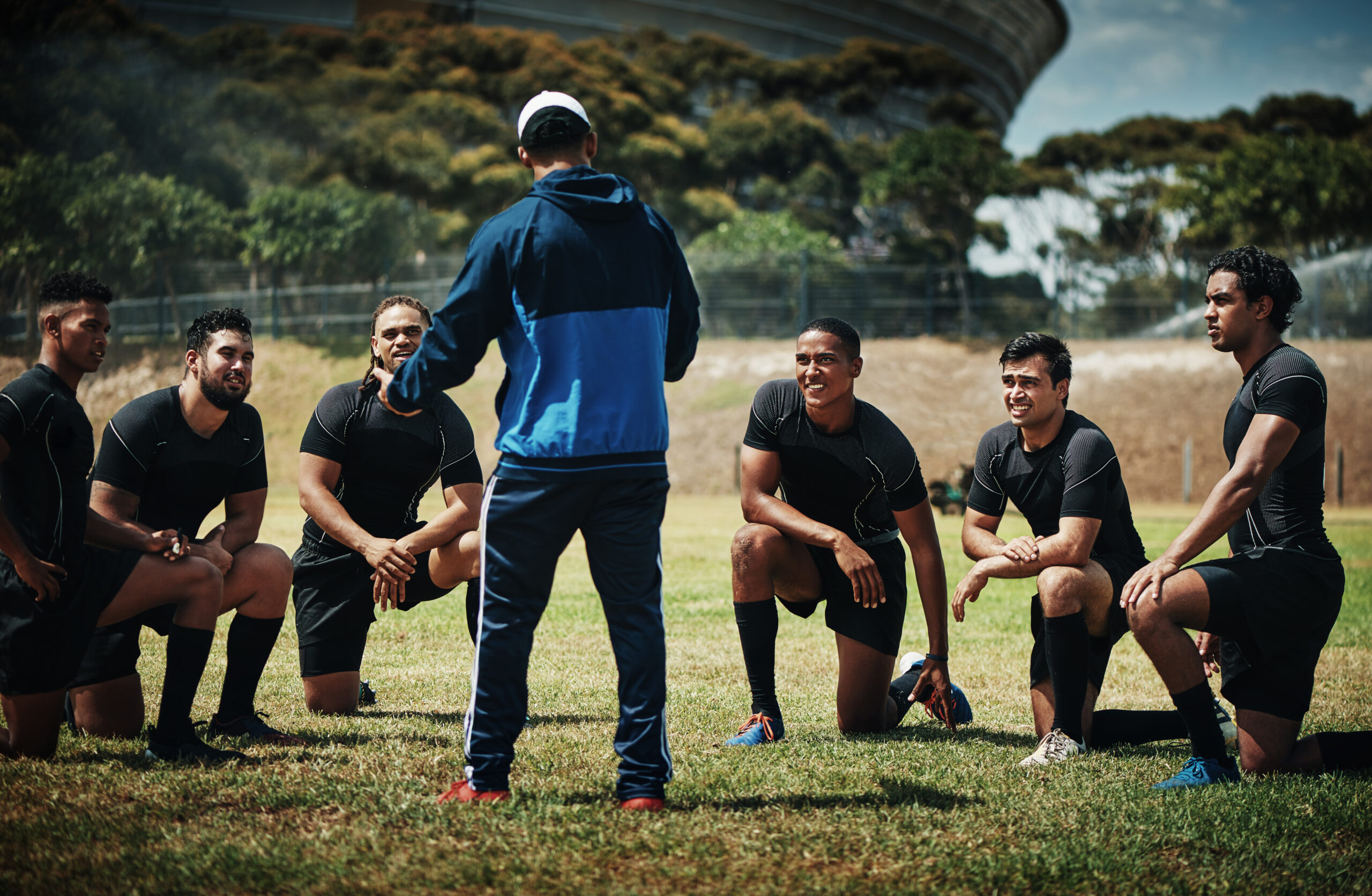 Cropped shot of a team of rugby players training with their coach on the field during the day.